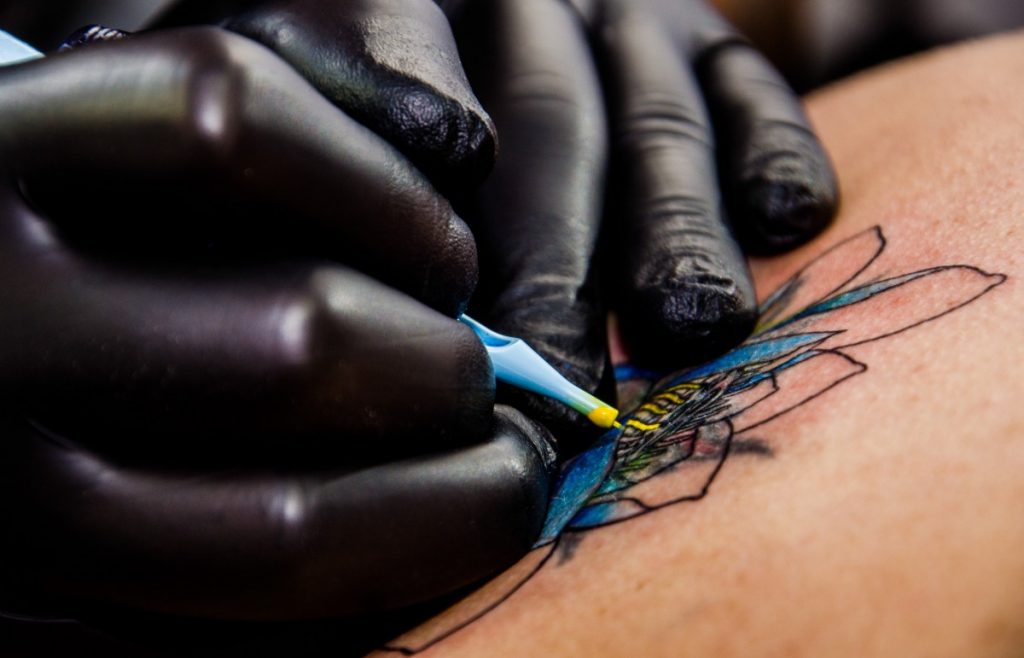 Tatoueur qui réalise un tatouage en couleurs d'une fleur de lotus