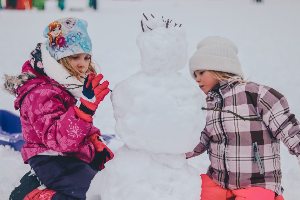 deux enfants habillés chaudement qui font un bonhomme de neige