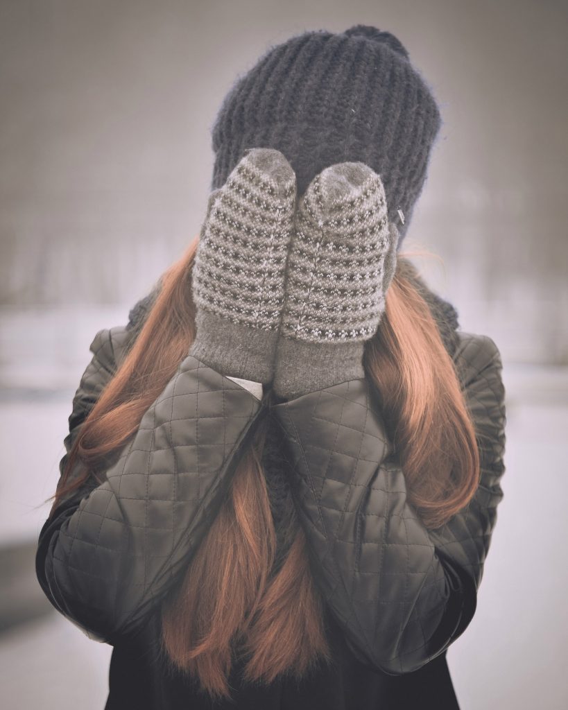 femme qui se cache le visage avec les mains portant des moufles et un bonnet