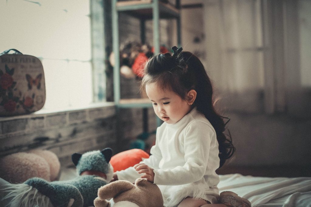 petite fille assise sur un lit qui joue avec ses doudous