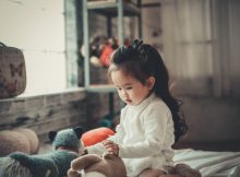 petite fille assise sur un lit qui joue avec ses doudous